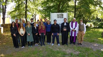 Eine Gruppe junger und älterer Menschen, die vor einer Tafel mit Text und Bildern stehen.