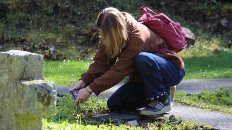 Ein Mädchen kniet auf dem Rasen und befestigt etwas vor einem Grabstein